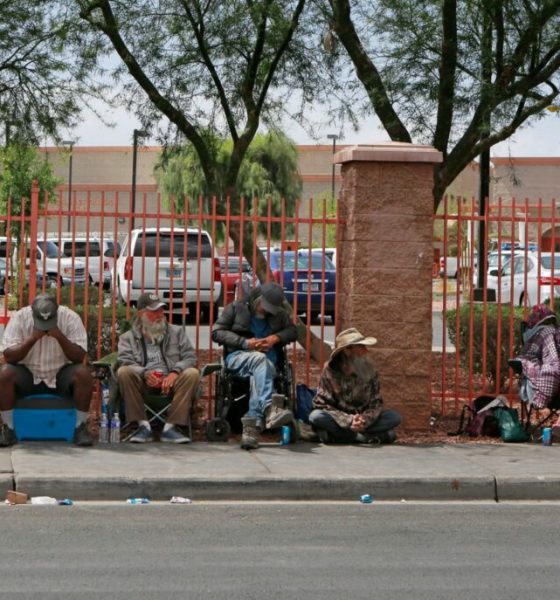 People sitting along sidewalk beside red fence