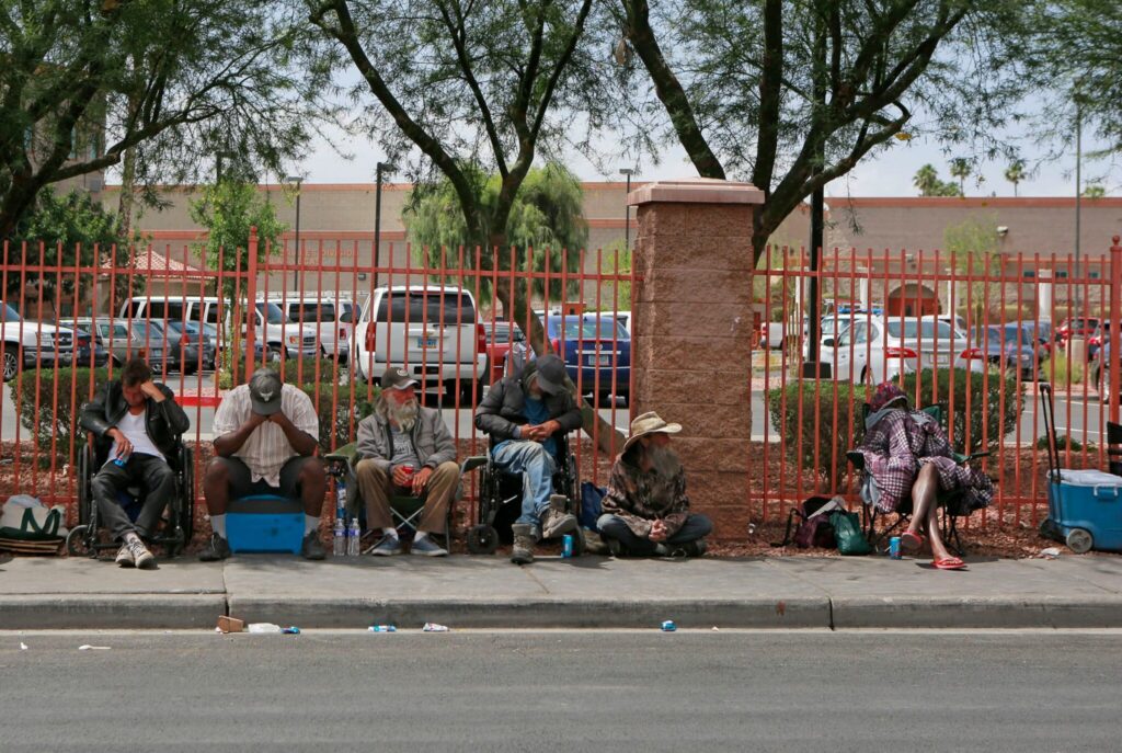 People sitting along sidewalk beside red fence