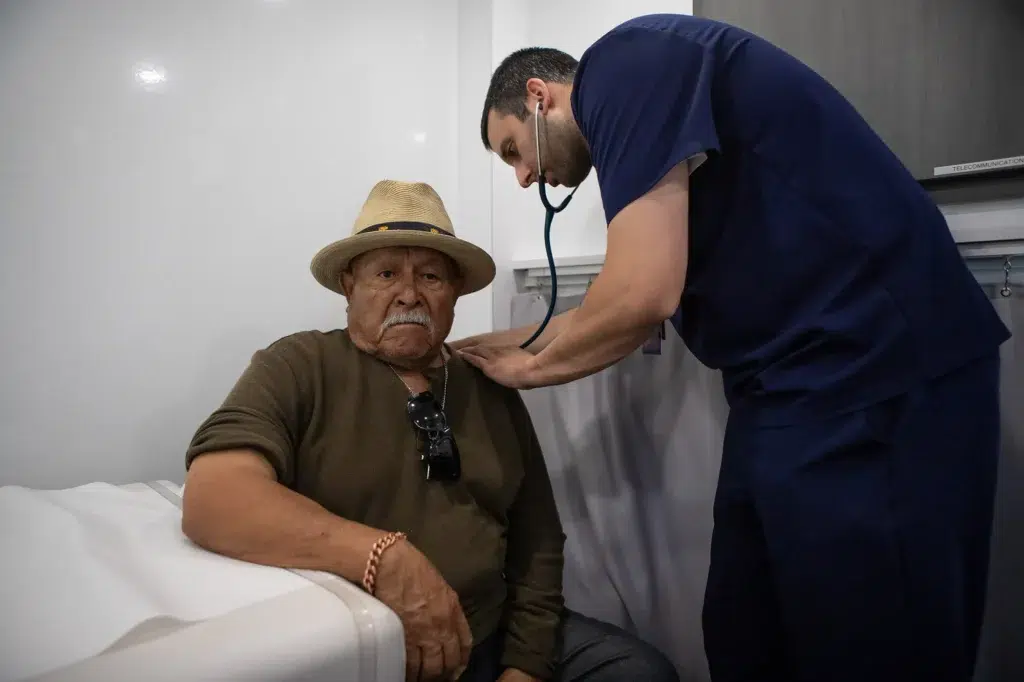 Doctor examining elderly patient with stethoscope in clinic