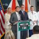 Officials and doctors at podium with U.S. flags