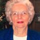 Elderly woman with white hair and glasses smiling