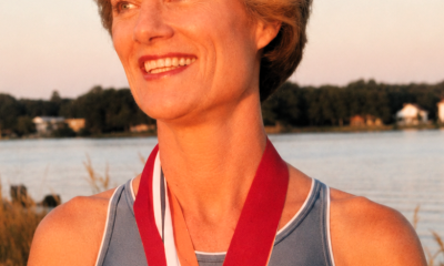 Smiling athlete wearing medals by lakeside at sunset