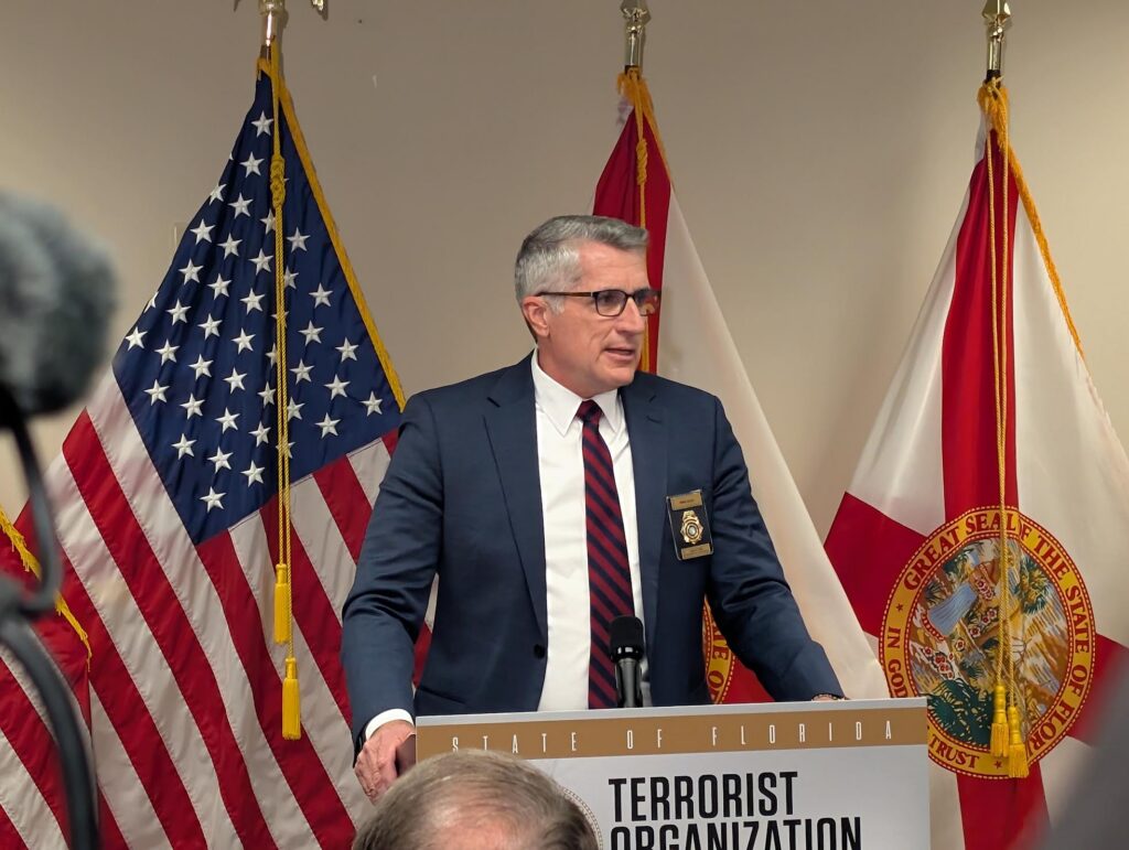Official speaking at podium with U.S. and Florida flags