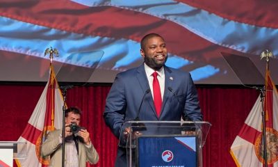 Man speaking at podium with American flag backdrop