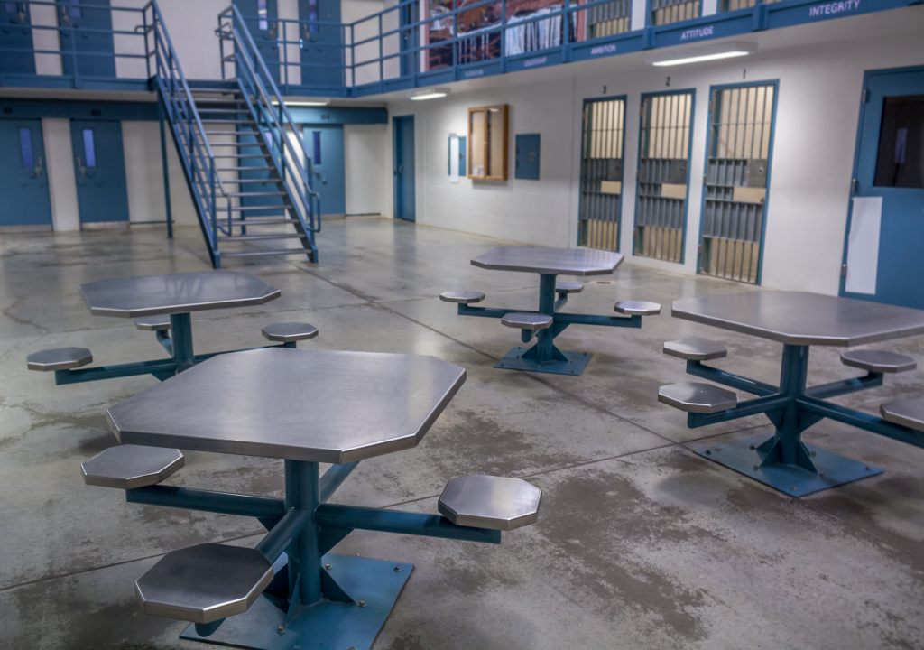 Empty prison common area with metal tables and cells