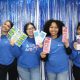 Four women holding educational pamphlets in front of blue backdrop