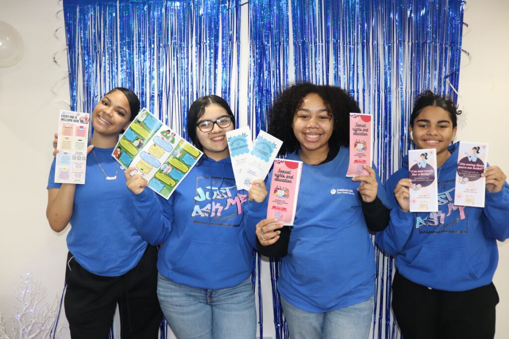 Four women holding educational pamphlets in front of blue backdrop