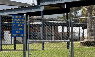 School campus behind chain-link fence with surveillance sign