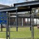 School campus behind chain-link fence with surveillance sign