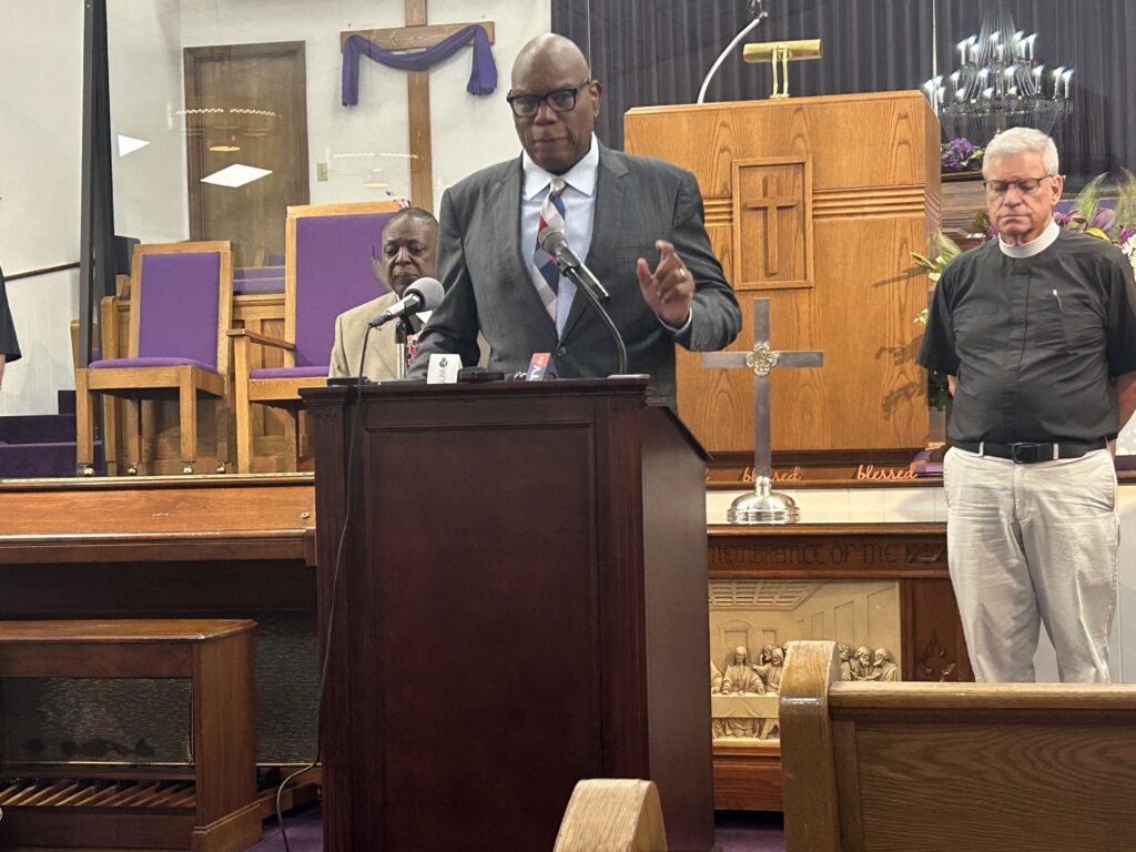 Man speaking at church podium with clergy