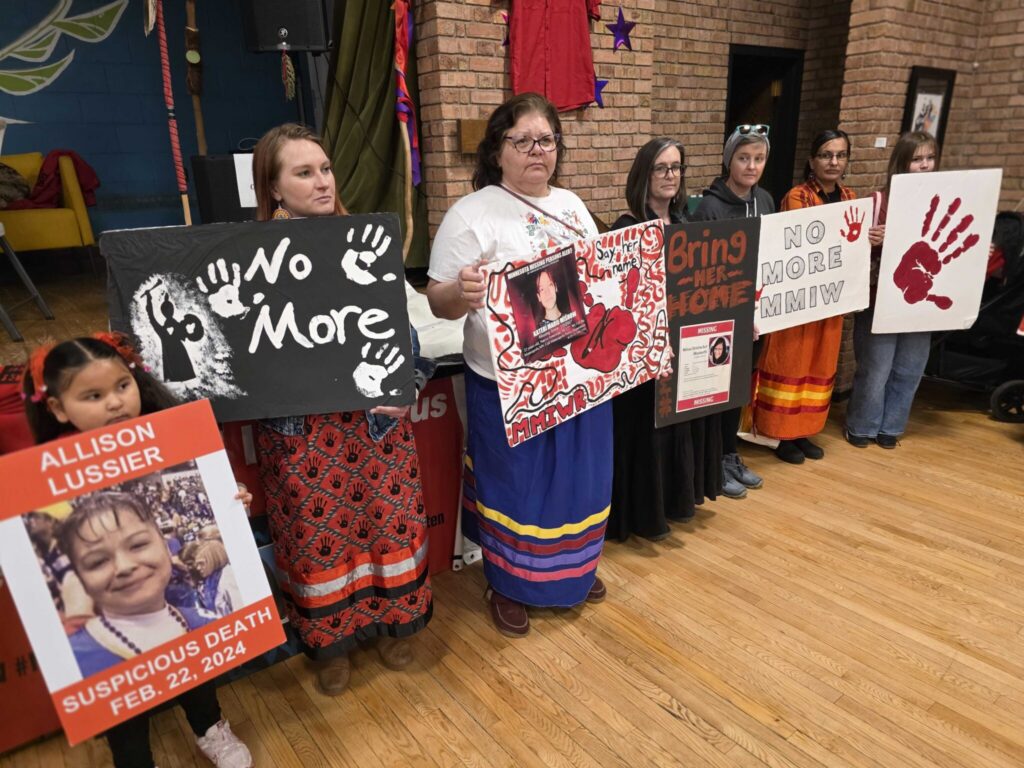Women holding MMIW protest signs indoors