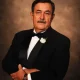 Man in tuxedo posing against brown backdrop