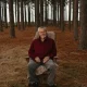 Older man sitting in chair in pine forest