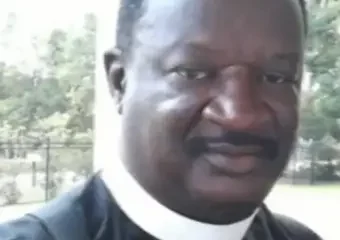 Man wearing clerical collar outdoors smiling at camera