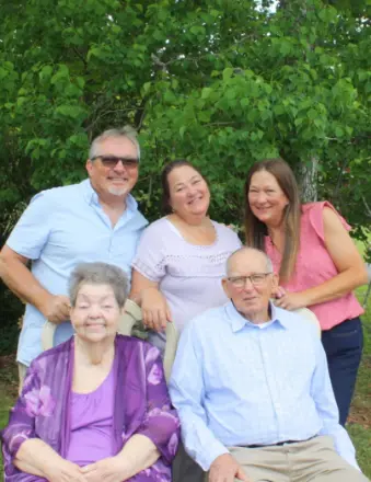 Multigenerational family portrait outdoors with greenery backdrop