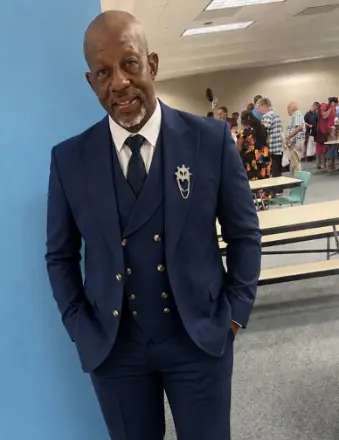 Man in navy suit leaning against wall