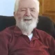 Elderly man with white beard smiling indoors