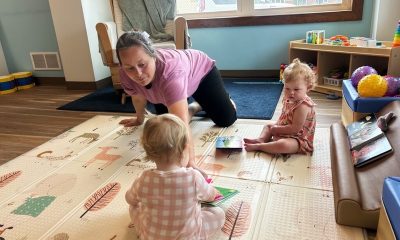 Caregiver playing with two toddlers on mat