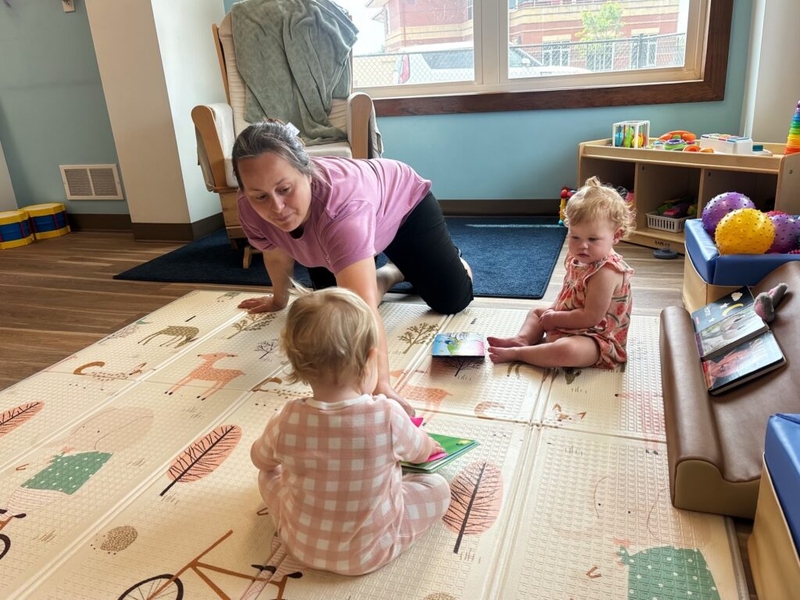 Caregiver playing with two toddlers on mat