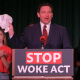 Man speaking at podium holding white cap