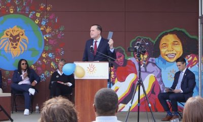 Man speaking at podium before colorful mural