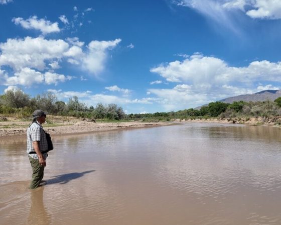 Man standing in shallow muddy river landscape — pensacola water costs climate change