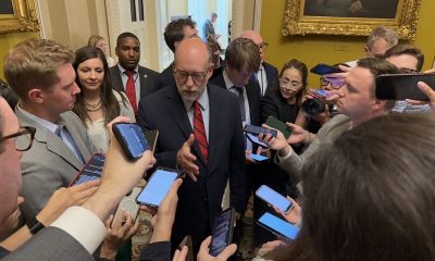 Man in suit surrounded by reporters indoors