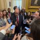 Man in suit surrounded by reporters indoors
