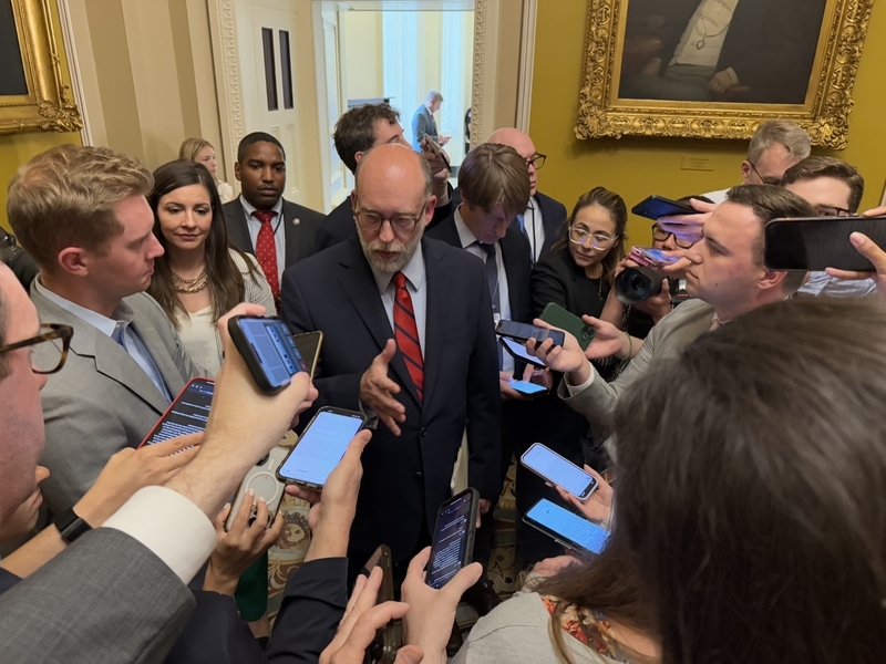 Man in suit surrounded by reporters indoors