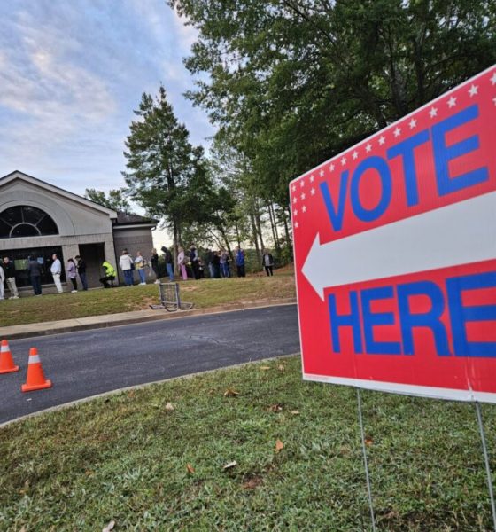 A bright red 'Vote Here' sign points towards a polling location with voters li — Northwest Florida election administration