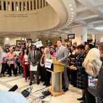 A diverse group of supporters holding signs gathers around a podium during a press confer — Florida school board elections
