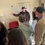 A group of people listening to a speaker in a room with a bullet hole in the wall — domestic violence death investigations