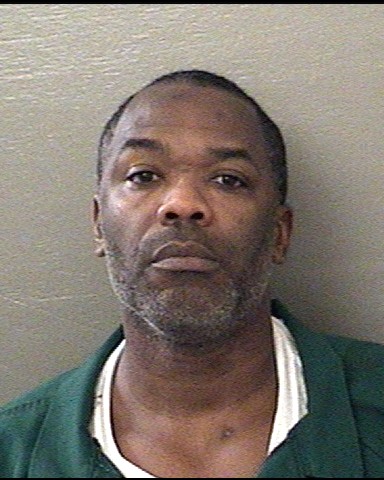 Mugshot-style portrait of a man in green shirt