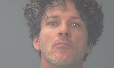 Mugshot-style portrait of curly-haired man in green shirt