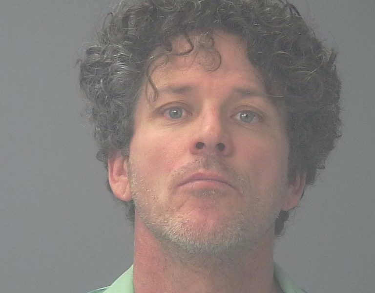 Mugshot-style portrait of curly-haired man in green shirt