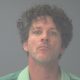 Mugshot-style portrait of curly-haired man in green shirt