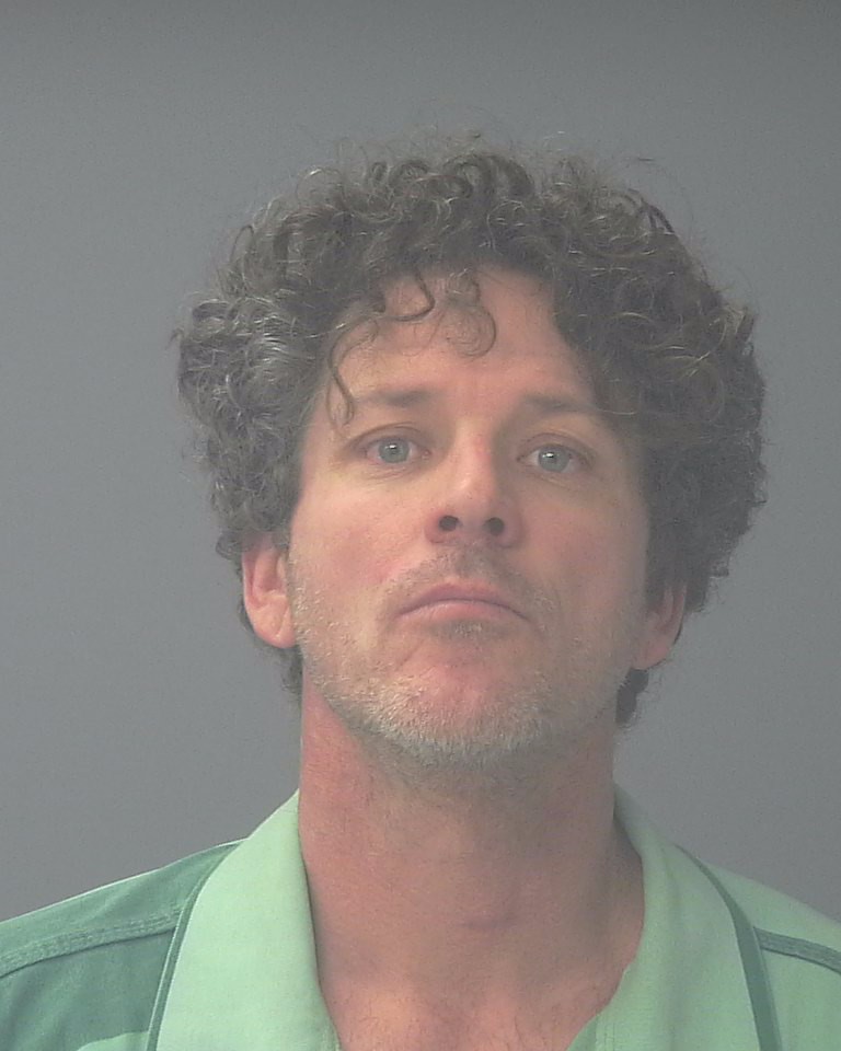 Mugshot-style portrait of curly-haired man in green shirt