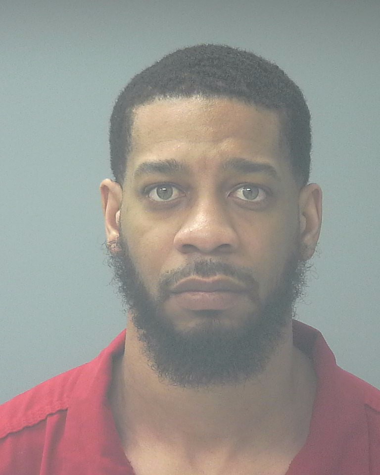 Mugshot-style portrait of bearded man in red shirt