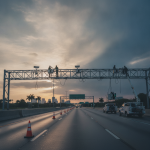 Workers dismantling FDOT license plate readers from an overpass on a Florida highway at sunset.