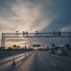 Workers dismantling FDOT license plate readers from an overpass on a Florida highway at sunset.
