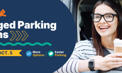 A smiling woman holding a coffee cup in a car, promoting new downtown Pensacola parking options starting October 5.