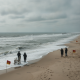 Lifeguards and beachgoers stand on a sandy beach with warning flags near rough ocean waves — corrientes de resaca Escambia