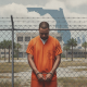 A man in an orange prison jumpsuit stands handcuffed in front of a Florida map si — illegal reentry federal prison Florida