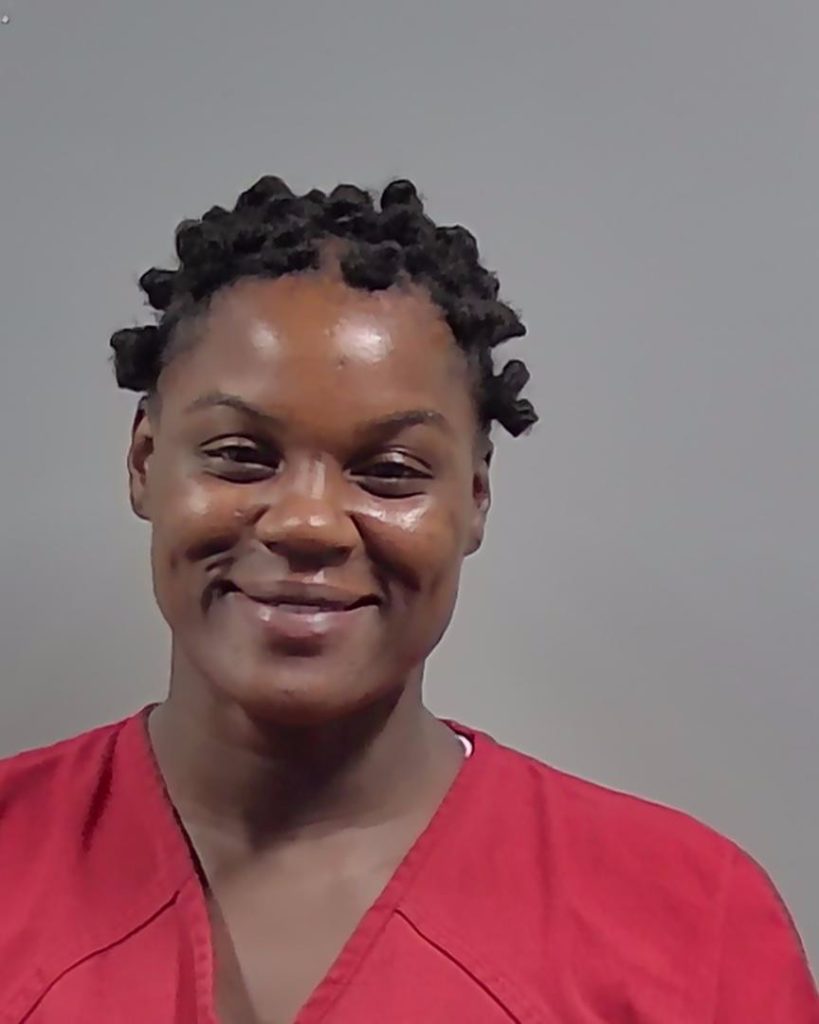 Mugshot of a Lisa Ann Elliot in a red prison uniform with short, curly hair, smiling slightly. — Cantonment shooting arrest