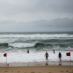 People wading in the ocean near red flags warning of dangerous rip currents in Pensacola. — corrientes de resaca Pensacola
