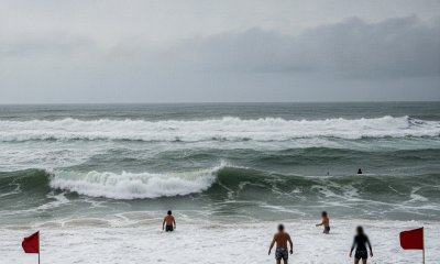 People wading in the ocean near red flags warning of dangerous rip currents in Pensacola. — corrientes de resaca Pensacola