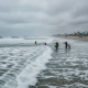 Surfers and beachgoers near turbulent waves on a cloudy day, highlighting the dangers of corrientes de resaca escambia.