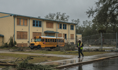 A worker walks past a boarded-up school building and a damaged yellow school bus after H — Escambia County School Closures