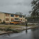 A worker walks past a boarded-up school building and a damaged yellow school bus after H — Escambia County School Closures