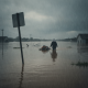 A person wades through floodwaters in a heavily inundated area, with houses partially submer — Escambia County flood watch